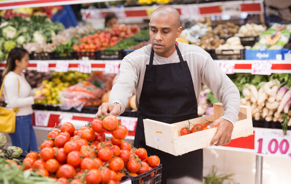 Seller in supermarket of Latin American origin checking tomatoes