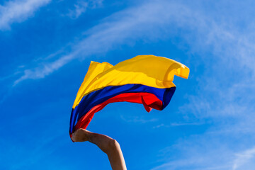 hand in fist at a protest in Colombia holding a Colombian flag with a blue sky background