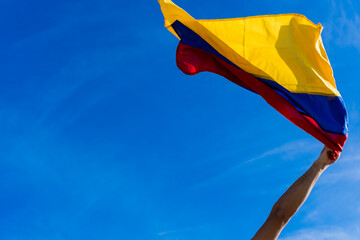 hand in fist at a protest in Colombia holding a Colombian flag against a blue sky background, copy space - obrazy, fototapety, plakaty