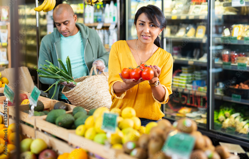 Wall mural married couple choosing ripe tomatoes at grocery store