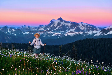 Woman walking in colorful alpine meadows with flowers  by snowcapped mountains at sunset.  Mount...