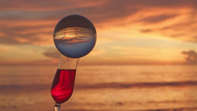Crystall ball set on the mouth of a red wine glass with a sea and beautiful sky at sunset background..A video for a unique and creative travel idea.4K clip