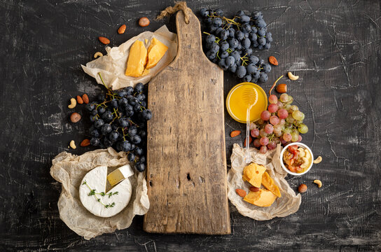 Empty wooden vintage cutting board in center of frame made of honey grapes cheese snack other ingredients gastronomy snacks. Mock up or copy space on cutting board for drink of wine bottle or food.