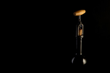 Red wine bottle with 2 glasses and bottle opener on black background.