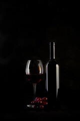 Red wine bottle with 2 glasses and bottle opener on black background.