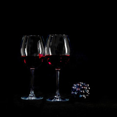 Red wine bottle with 2 glasses and bottle opener on black background.