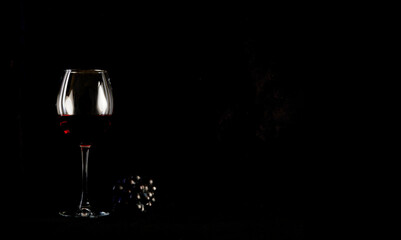 Red wine bottle with 2 glasses and bottle opener on black background.
