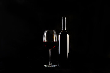 Red wine bottle with 2 glasses and bottle opener on black background.