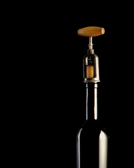 Red wine bottle with 2 glasses and bottle opener on black background.