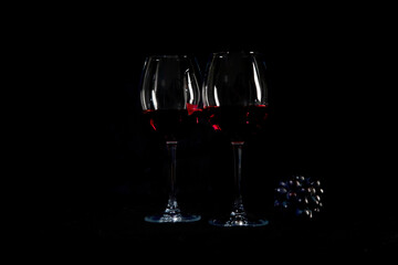 Red wine bottle with 2 glasses and bottle opener on black background.