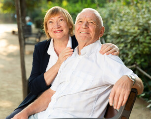 Portrait of senior couple in love sitting on bench in park on sunny day