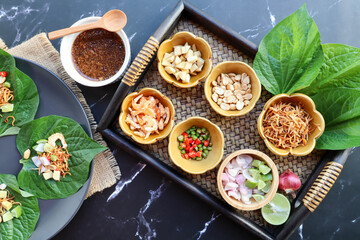 Thai appetizer of food and herb wrapped in leave dipping with sweet sauce in Thai food called Miang Kham - Top view on dark marble background