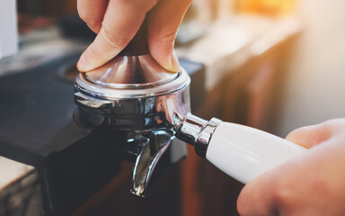 Closeup image of barista using a tamper to press ground coffee into a portafilter in coffee shop