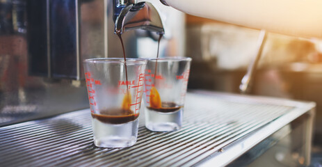 Closeup image of espresso pouring from coffee machine into shot glasses