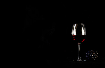 Red wine bottle with 2 glasses and bottle opener on black background.