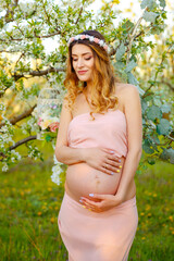 Fototapeta na wymiar Beautiful pregnant woman relaxing in the park. Happy pregnant woman in pink dress looking at sunrise. Enjoying healthy pregnancy. Smiling pregnant woman in rural landscape. Maternity, pregnancy care.