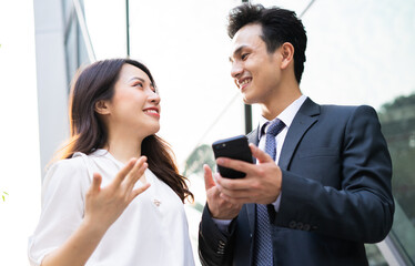 Two Asian business people using smartphone and talking together