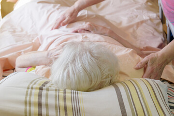 Caregiver's arms embrace a bedridden elderly person. The woman lies in a medical bed. White hair....