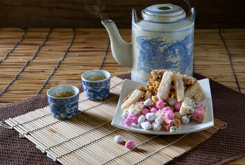 Chinese dessert in white dish and tea in white cup with old teapot  all put on the bamboo mat and old wooden wall ,