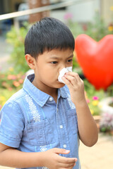 An Asian boy blowing his nose into a tissue.