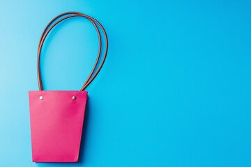 Paper shopping bag with round handles on a blue background. Flatlay with space to copy. Fashionable solid pink handbag. Mockup.