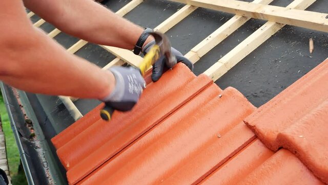 Skilled roofer nailing red concrete roof tiles on residential house.