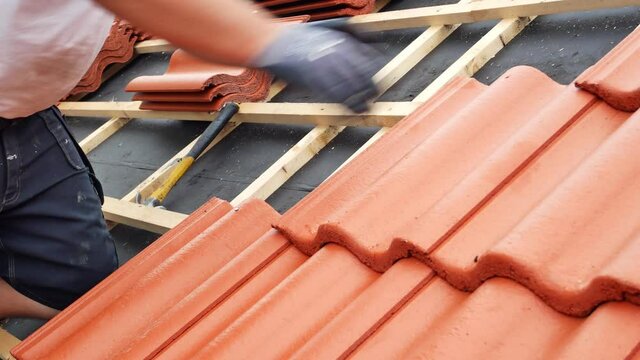 Professional roofer fitting red concrete roof tiles on  residential house.