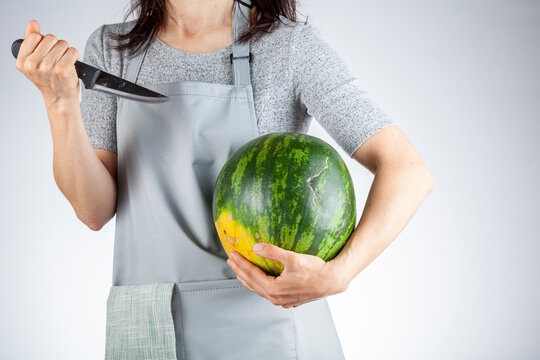 A caucasian woman is preparing to stab a watermelon using a sharp kitchen knife. A versatile image for summer fruits as well as a demonstration of force, metaphorical passive aggressive behavior