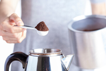 A caucasian woman is taking a teaspoon of ground coffee from a jar using a plastic measuring spoon...