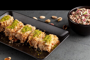 Turkish tel kadayif dessert made from shredded phyllo dough mixed with walnuts. It is sweetened with thick syrup and ground pistachio is added on top for decoration and flavor. A plate with ingredient
