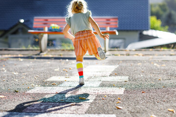 Cute little toddler girl playing hopscotch game drawn with colorful chalks on asphalt. Little...