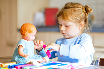 little alone toddler girl painting with felt pens during pandemic coronavirus quarantine disease. Happy creative child with old vintage doll, homeschooling and home daycare with parents