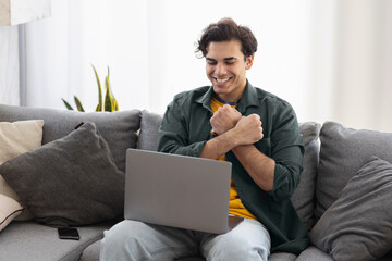 Deaf or hard hearing happy smiling young caucasian man uses sign language while video call using laptop while sitting on the couch at home