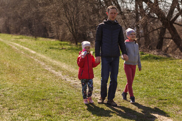 Young father with two daughters walking in nature. A man with two children are walking on the trail. Dad holds children by the hands.