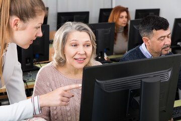 Portrait of happy mature woman studying together with young female coach in university computer class