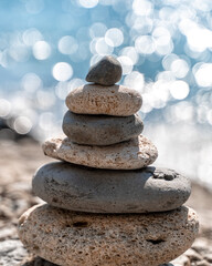 Fototapeta na wymiar A tower of stones. Balanced pyramid of pebbles on the beach on a sunny day. Blue sea in the background. Selective focus, bokeh. Zen stones on the sea beach, meditation, spa, harmony, tranquility