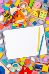 Colorful educational wooden plastic and fluffy baby kids toys and blank notebook with colored pencils on gray background. Top view