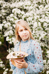 Girl holding a hat with flowers, spring walk, forest and trees, blue dress