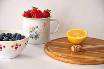 Healthy berry fruits with honey and lemon on white background