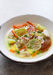 Bowl of soup with cod, carrots, potatoes and green peas close up