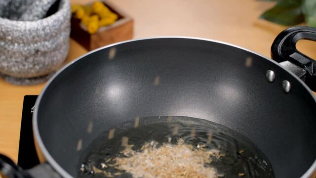 Closeup shot of an Indian woman's hand adding cumin seeds (Jeera) in hot oil. Hands of a female chef preparing the base for an Indian masala mix by adding cumin seeds - food cooking concept