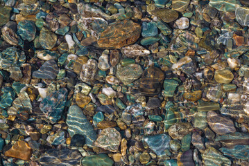Colorful pebbles at the bottom of a shallow river on a sunny day