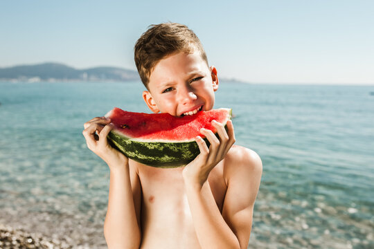 Cheerful child eating juicy watermelon on the sea.