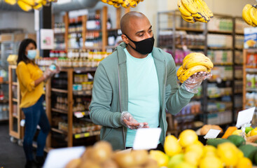 Man in protective mask picks ripe bananas at grocery supermarket