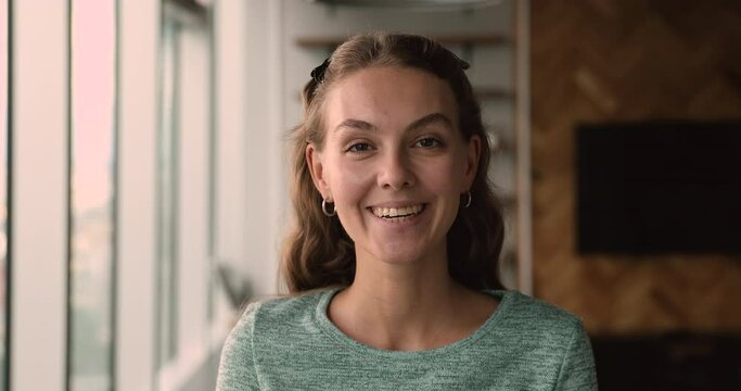 Head shot young female office manager standing alone in modern office room smiling look at camera. Happy intern and first workday in company, portrait of professional services supplier person concept
