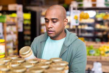 Adult positive man is choosing conserve in grocery supermarket