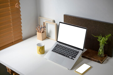 White office desk with laptop, coffee cup, smart phone, houseplant and pencils holder.