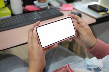Close up view of woman holding horizontal smart phone while sitting a her workplace.
