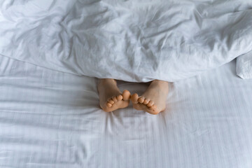 Morning and waking up. Feet under the covers in bed in the morning. Women's feet under the covers in a white bed. Relax, sleep, rest concept.