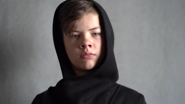 Unhappy teenage boy wearing black hoody looks at camera